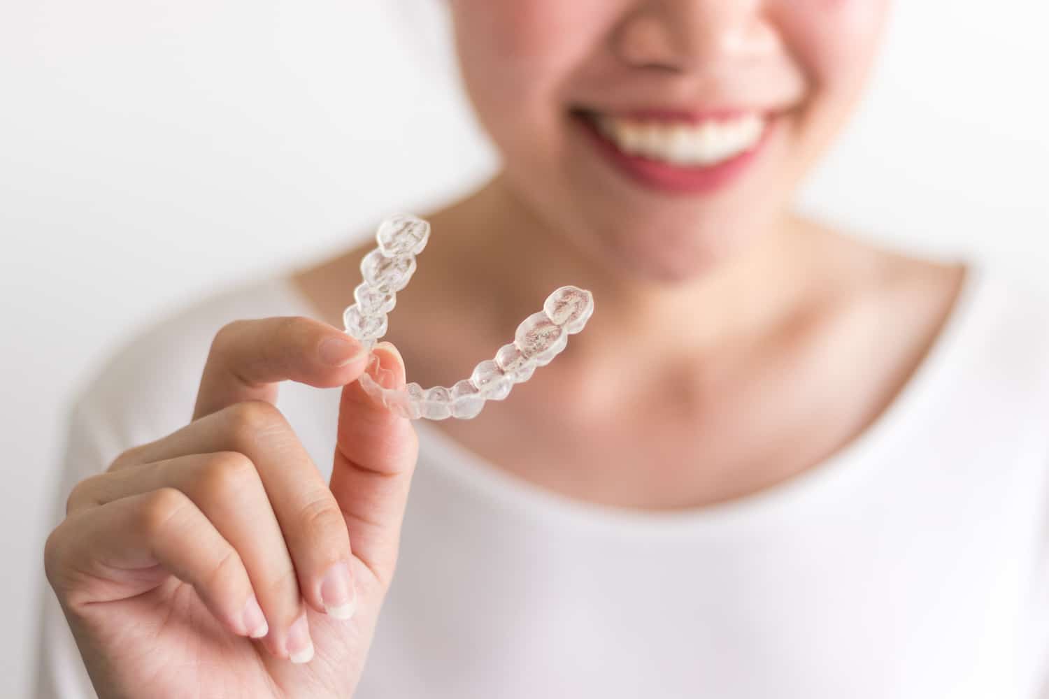 invisalign vs veneers woman smiling and holding out dental tray