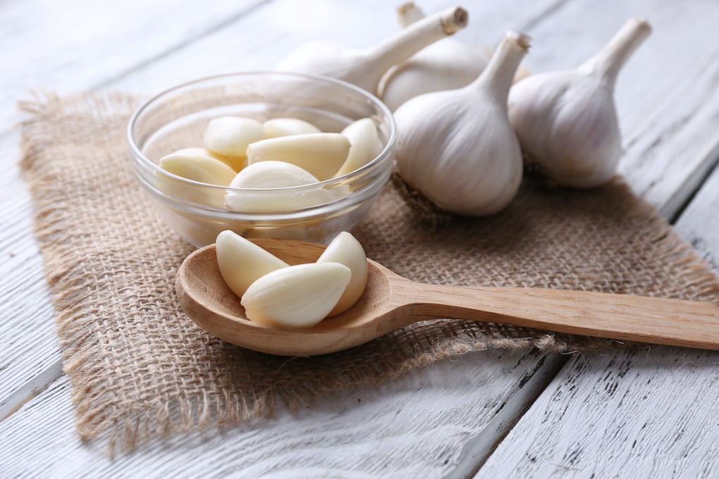 Fresh sliced garlic in glass bowl on wooden background; emergency toothache relief