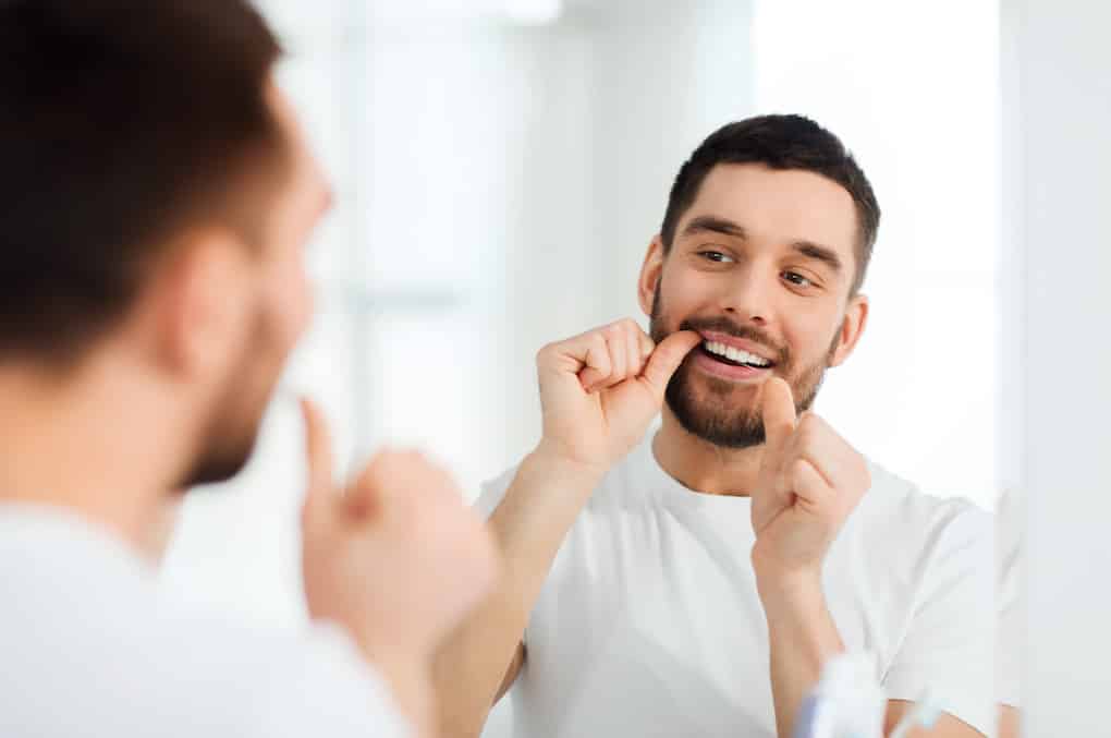man with dental floss cleaning teeth for gum health