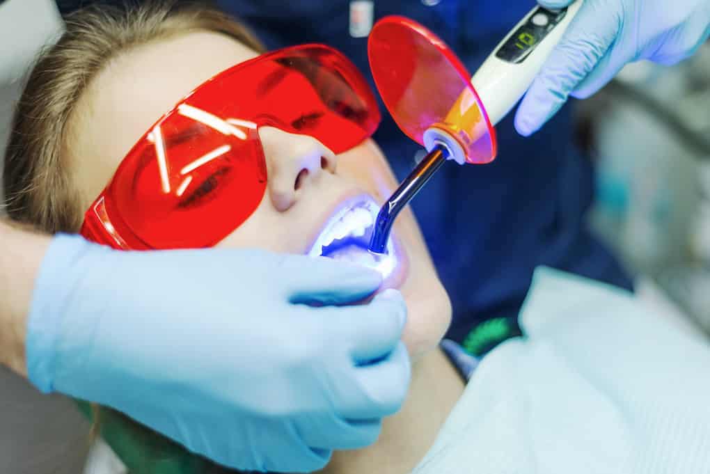 woman wearing glasses getting dental laser treatment; dental laser treatment side effects